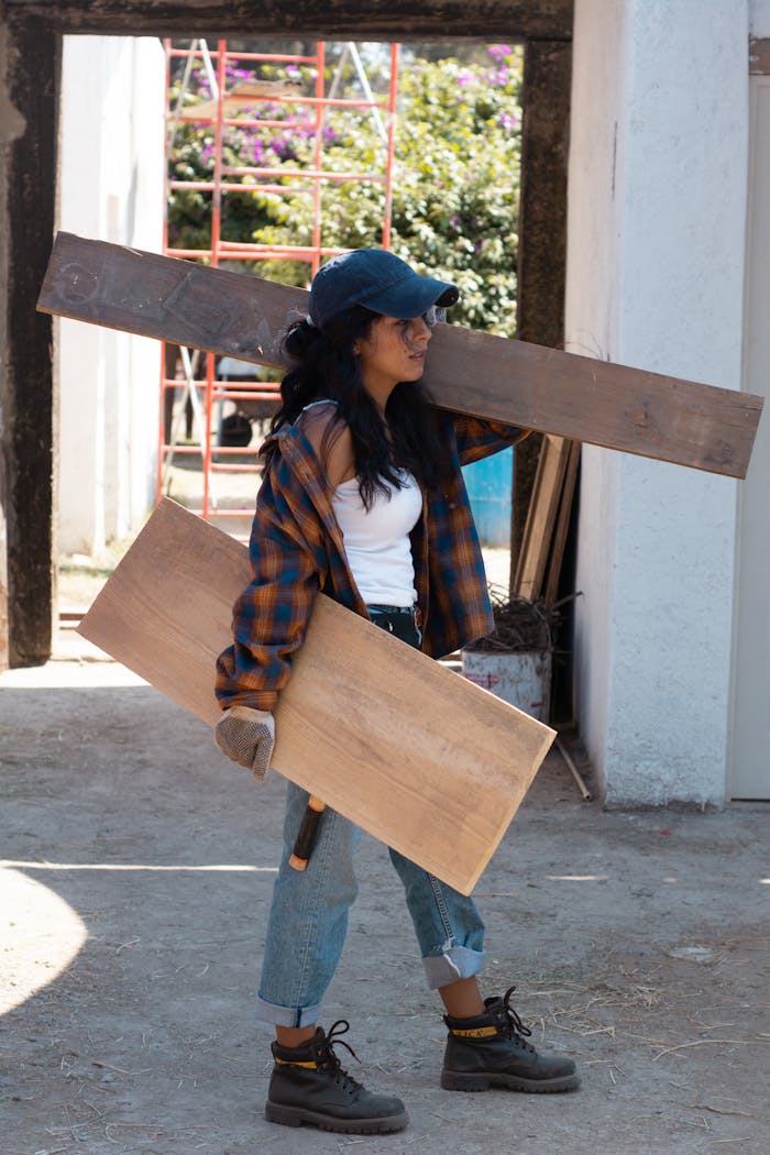 Young female carpenter in casual attire handling wooden planks at a construction site outdoors.